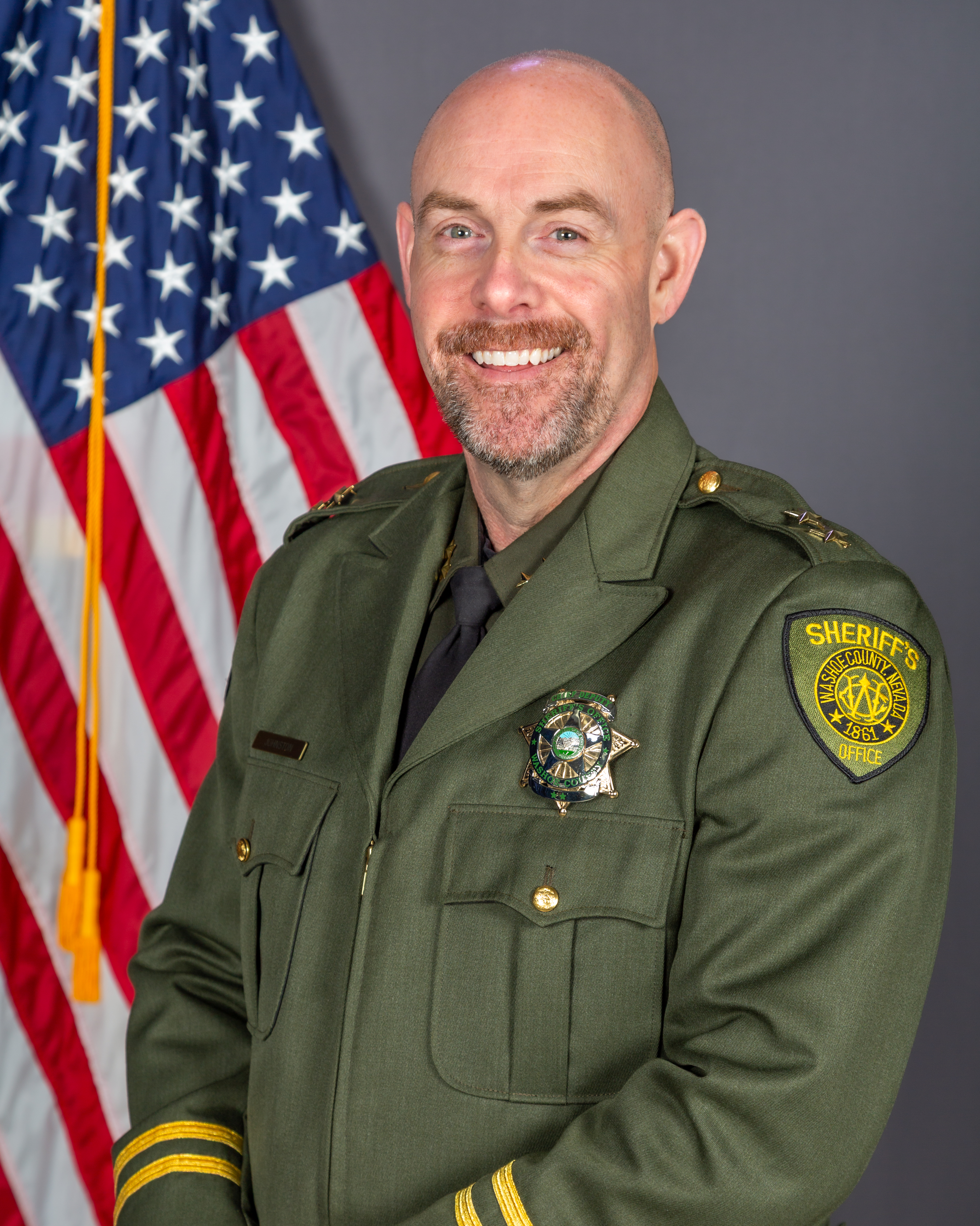 Assistant Sheriff Ryan Johnston, in WCSO uniform, poses in front of the American Flag
