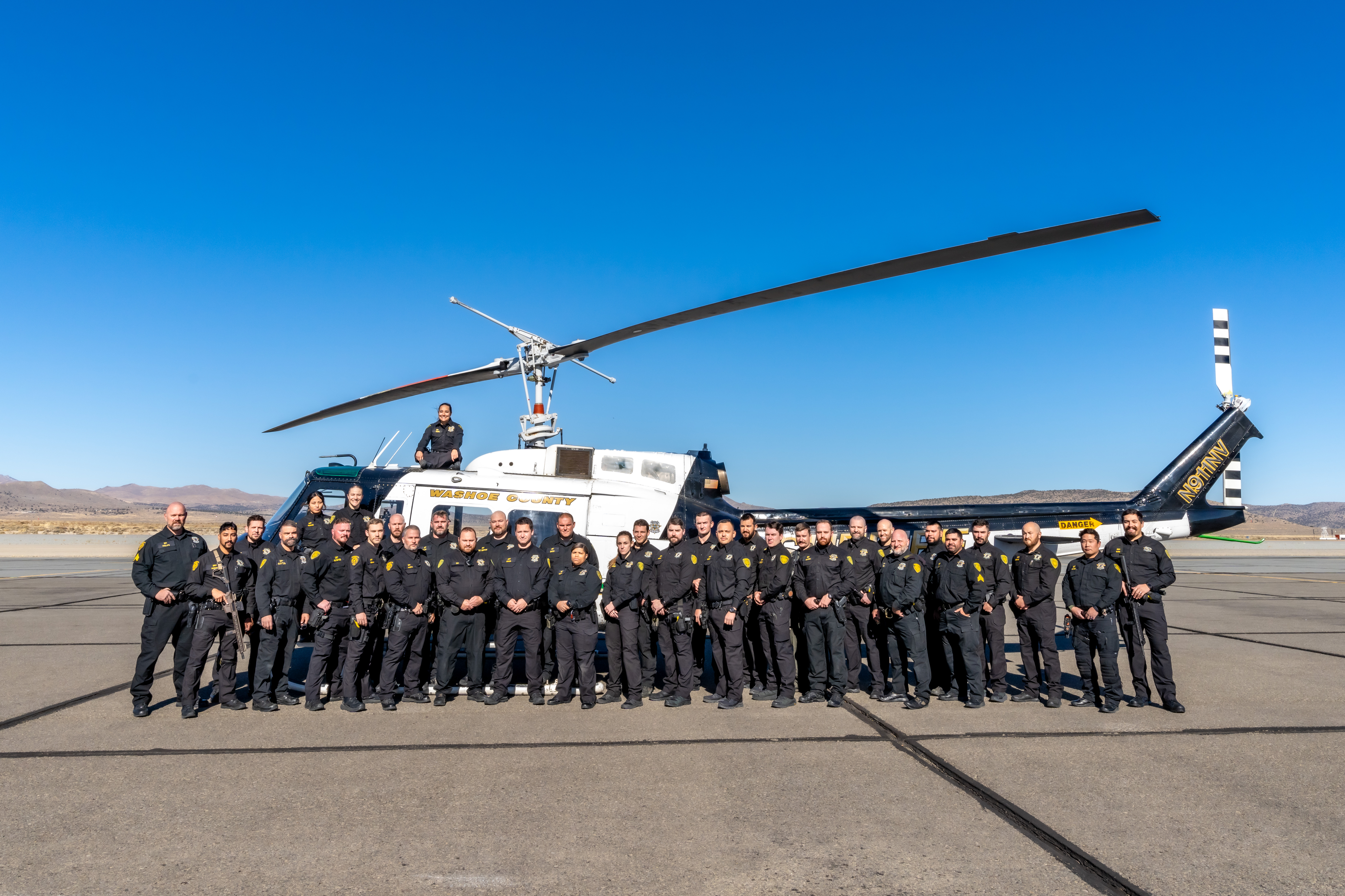 35 members of the Washoe County Detention Response team stand, in uniform, with the Regional Aviation Enforcement Unit (RAVEN) helicopter.