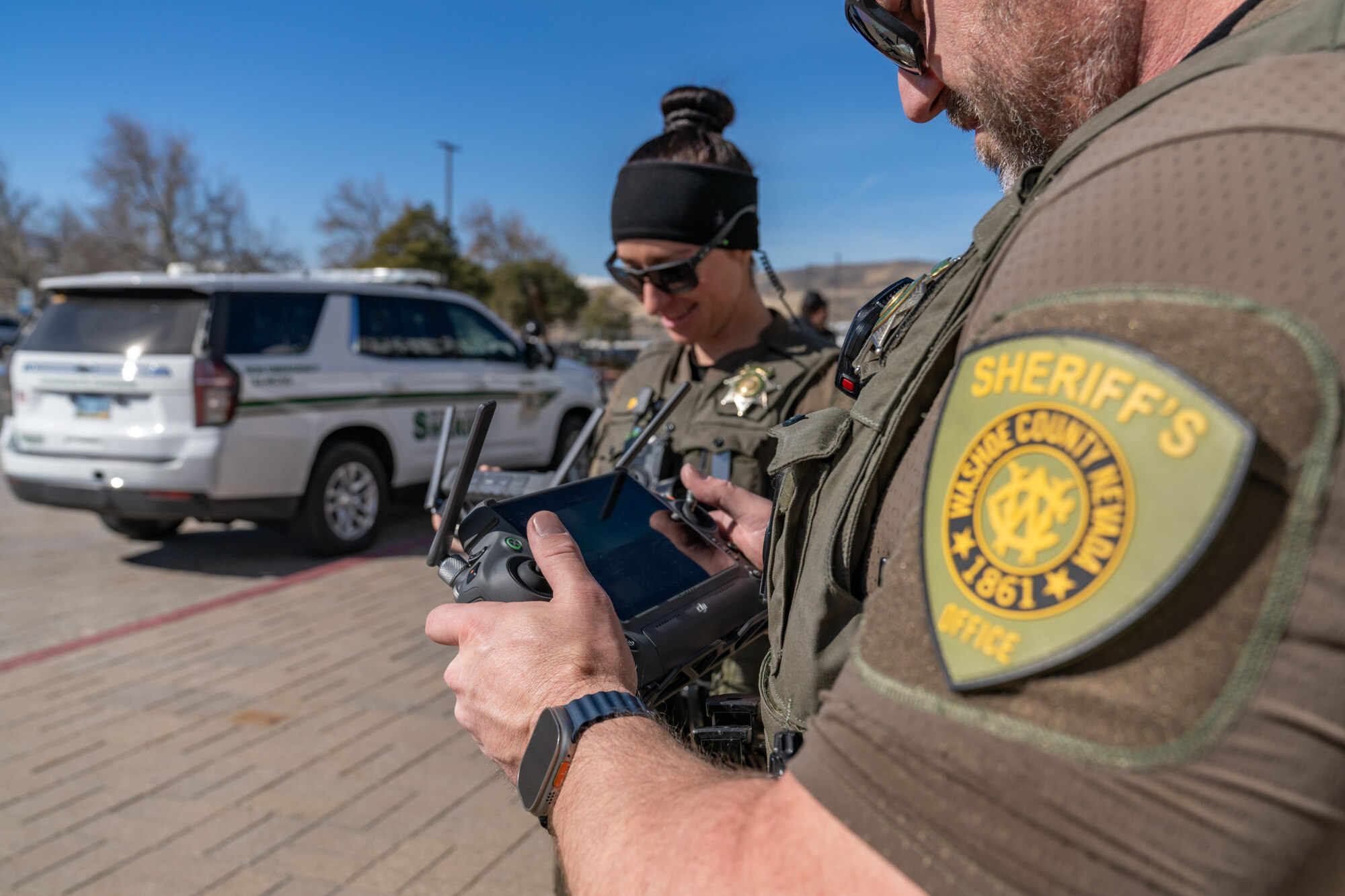 Two WCSO personnel conducting a drone demonstration, viewing the mobile control screen while operating drones in the field.